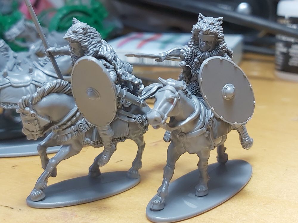 a photograph of two unpainted Victix miniature roman cavalry, with wolf pelts over their helmets