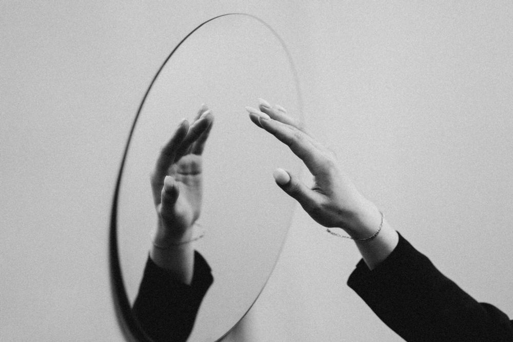 B&W photo of a mirror reflecting a hand reaching towards it.