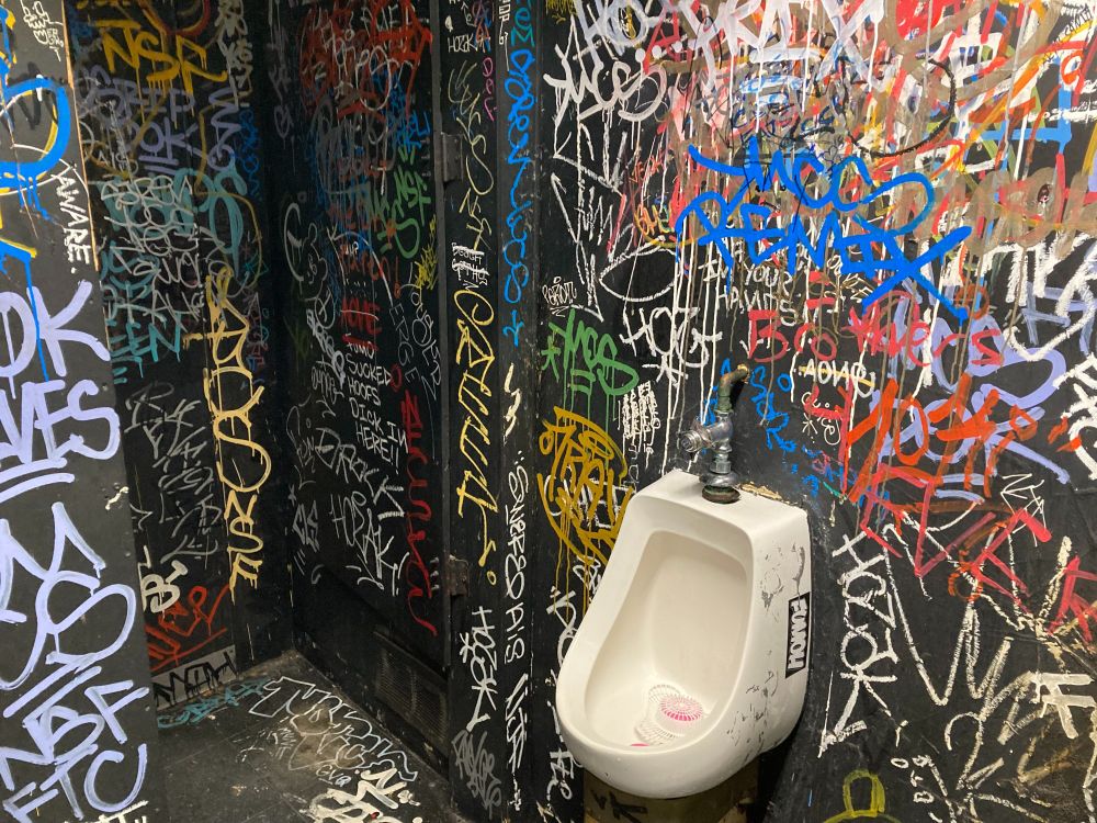 Eine Männertoilette in einem Pub in Pittsburgh. Die schwarzen Wände sind mit bunten Schriftzeichen übersät und geben dem Ambiente einen durchaus chaotischen Touch.