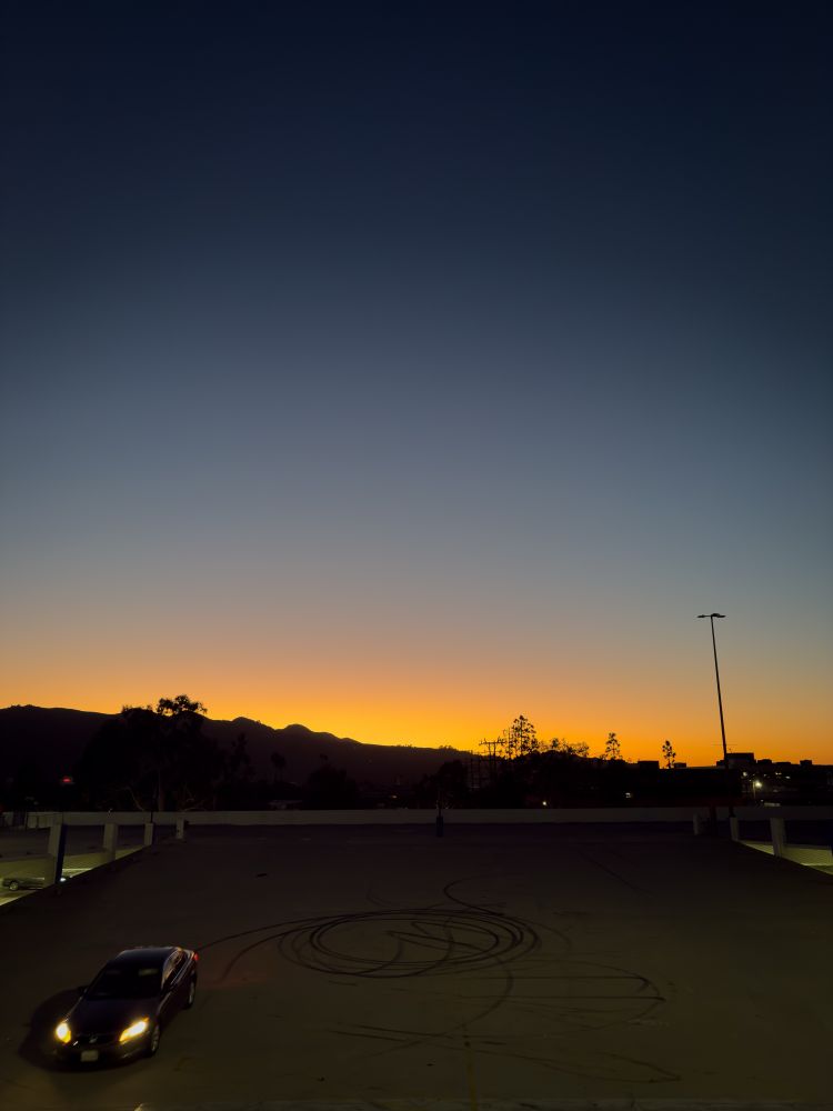 A car is heading down the top floor ramp of the Galleria parking lot, the sun is setting behind the hills in Glendale, CA