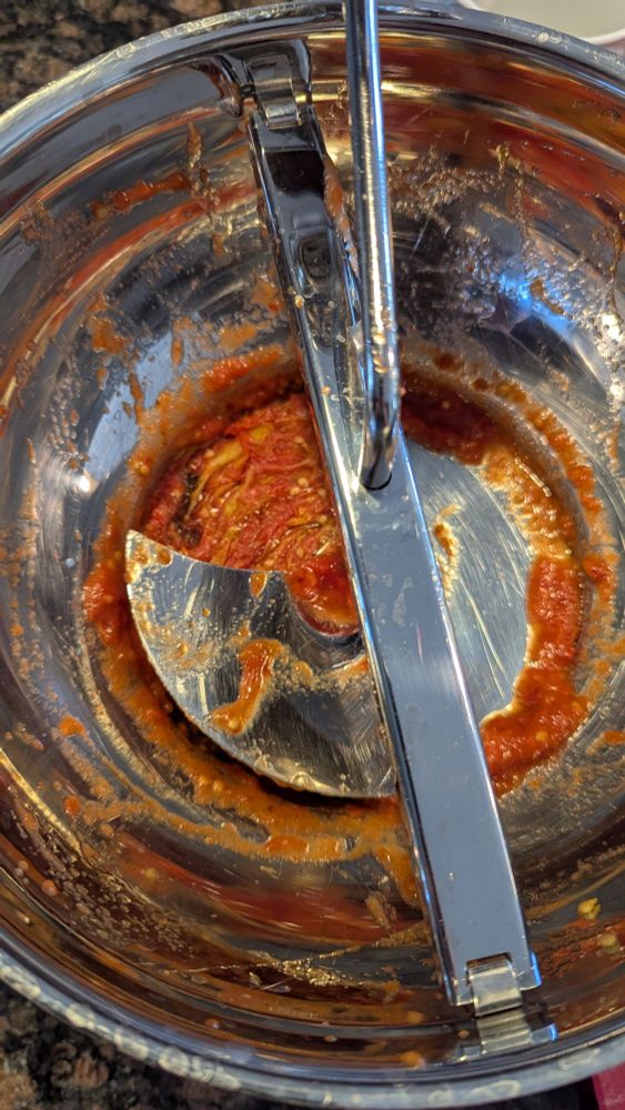 A stainless steel food mill has the remains of the roasted tomatoes inside from making sauce.