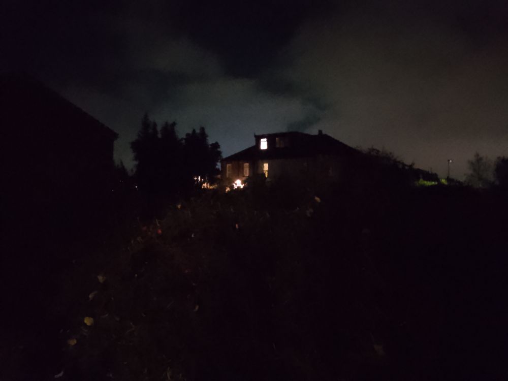 House with a few lights burning at dusk, seen from behind a hedge.