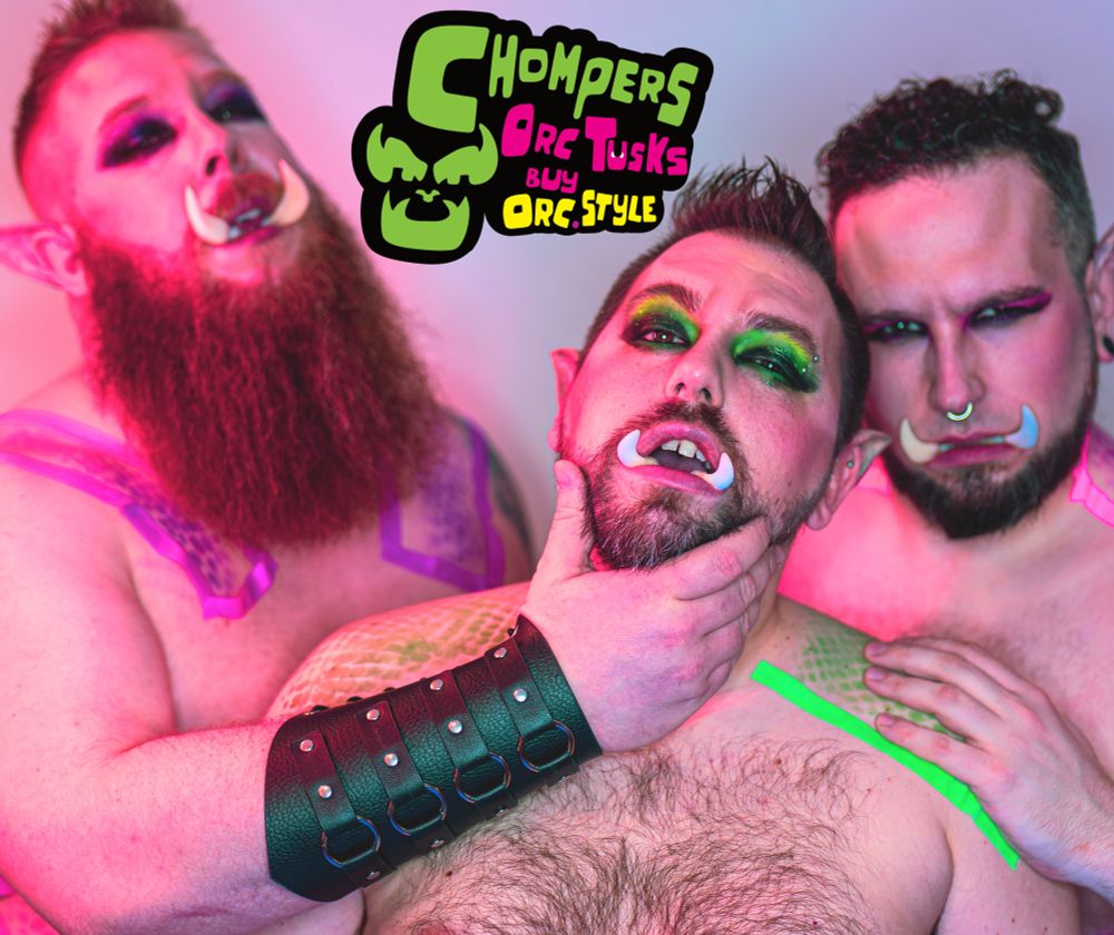 Three orcs stare seductively at the camera. Each has a unique set of cosplay orc tusks on and dramatic drag makeup with neon accents on each. One orc holds the jaw of the other in a horny manner.  