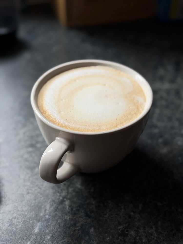 A latte in a white mug on a dark countertop. 