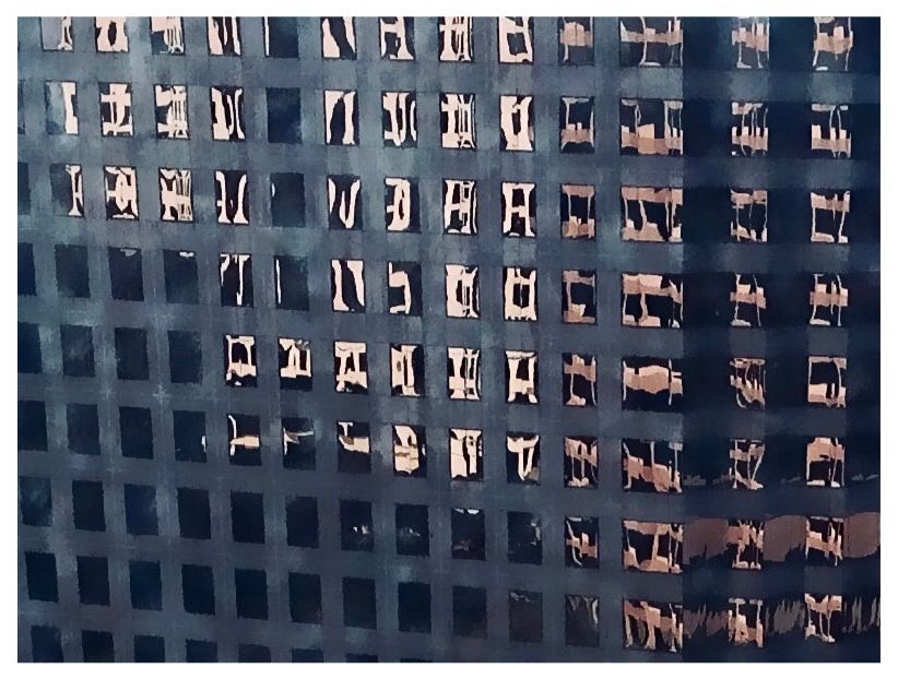 Color photo of two buildings reflected in the windows of a third. 