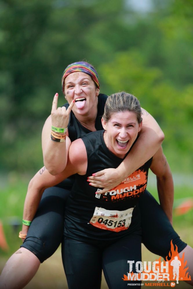 Cori riding on the back of a fellow racer during on of her Tough Mudder competitions. 
