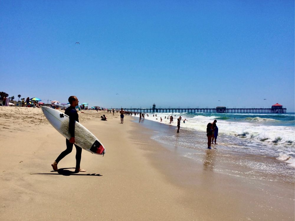 Color photo of a lone surfer carrying his board toward the surf. 