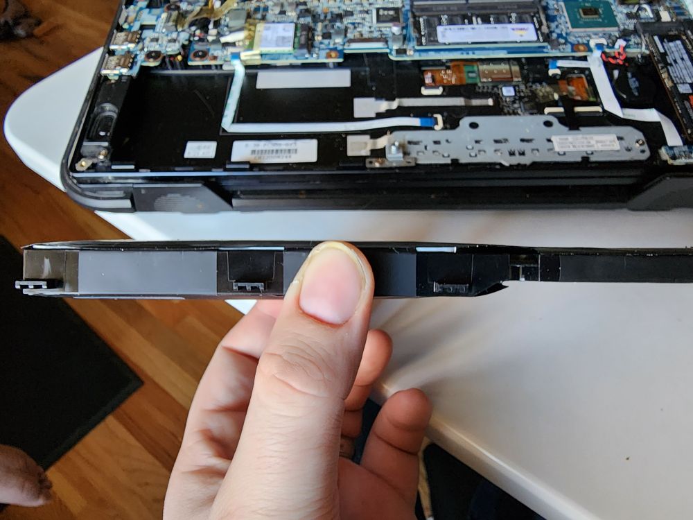A side view of a laptop battery module that has clearly expanded a few millimeters. The laptop mainboard is visible in the background.
