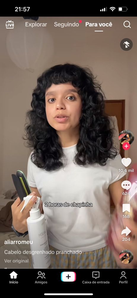 print de um video no tiktok que mostra uma jovem de cerca de 20 anos, com os cabelos pretos ondulados, de franja. ela veste uma camiseta branca e segura alguns produtos de cabelo. na legenda do video podemos ler "Cabelo desgrenhado pranchado"