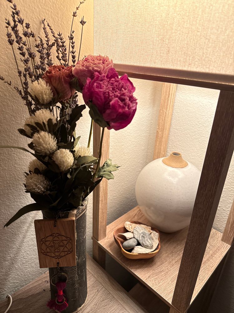 Two ceramic vases with a lamp, a wooden bowl of rocks and shells. Flowers both fake and dried sit in the vase with a handmade wooden talisman by Cen