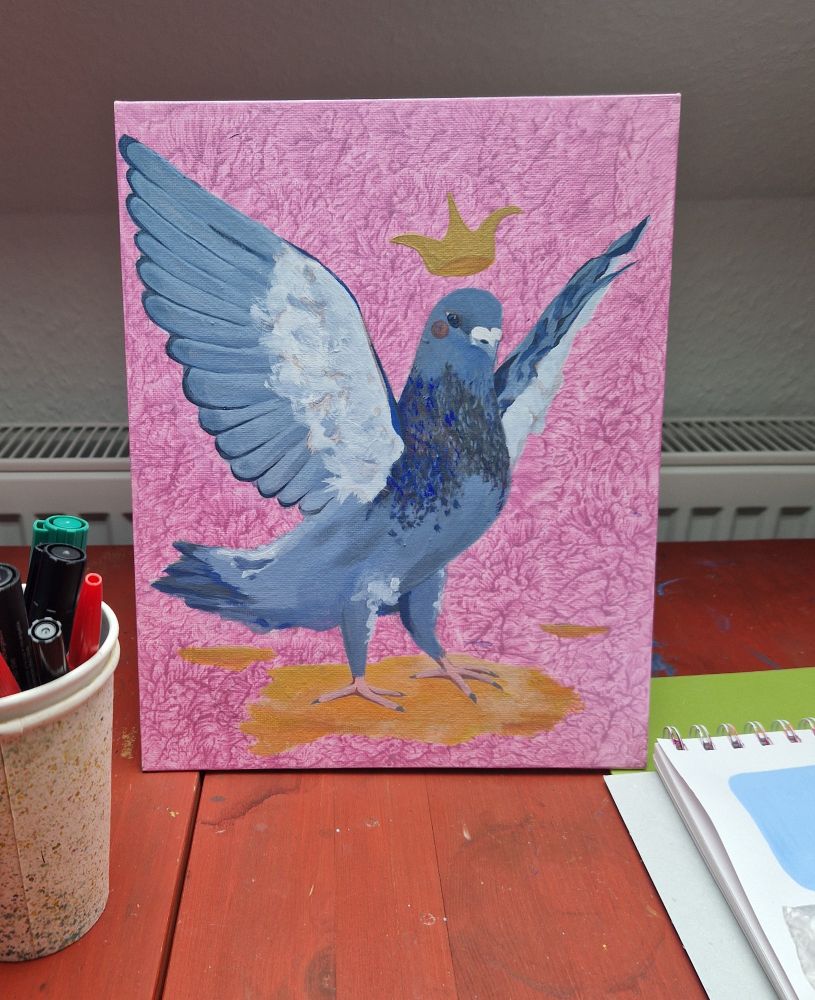 Tisch mit einem Becher Stifte, rechts der Anschnitt eines Skizzenblocks. Zentral steht eine A4 Leinwand mit pink-meliertem Hintergrund. Darauf ist eine Taube gemalt die ihre Flügel bereit zum Flug aufspannt und über deren Kopf eine Krone schwebt. Der Hintergrund und einzelne Details sind mit Glitzerpigmenten in der Farbe versehen.