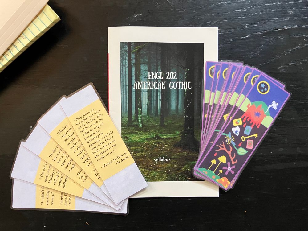 booklet-style syllabus for American Gothic with a haunted forest cover and laminated bookmarks with colorful cut-paper design —some are fanned out to show different quotations on the flipside from Jackson’s HAUNTING OF HILL HOUSE, Jones’ ONLY GOOD INDIANS, King’s SHINING, McDowell’s AMULET, and Moreno-Garcia’s MEXICAN GOTHIC