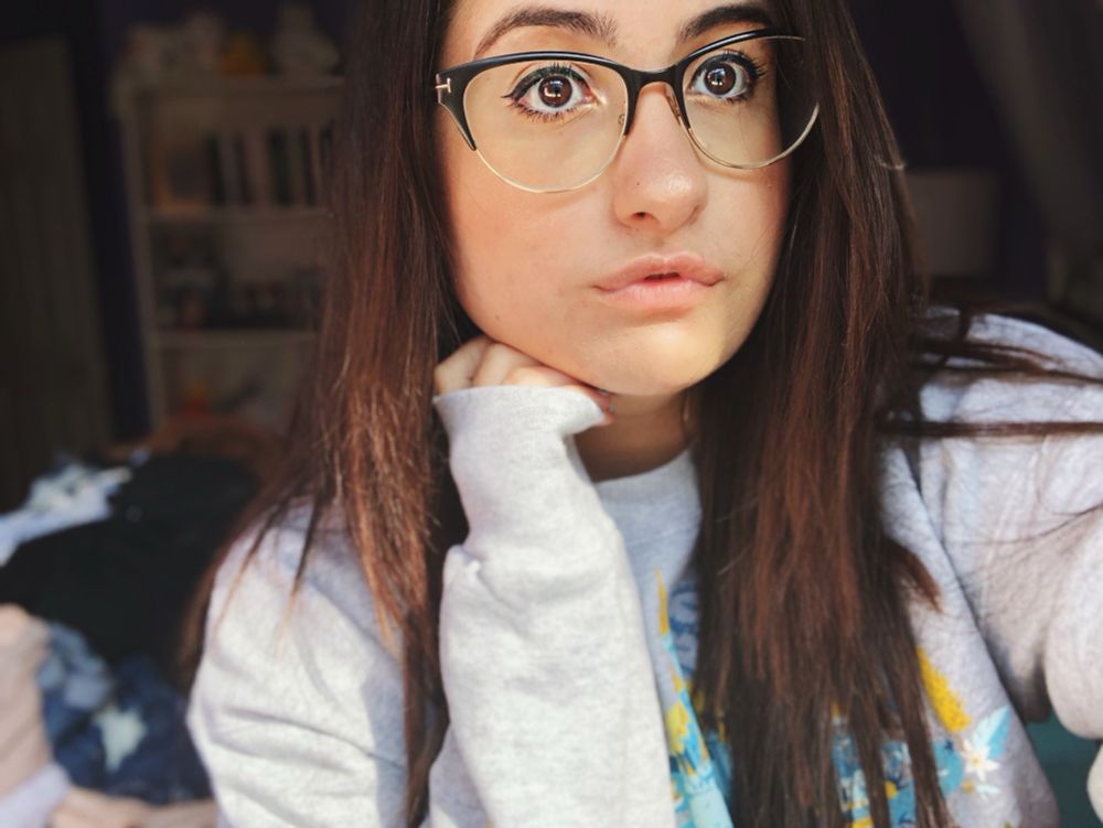 Almost 25 year old Shelby in her hair extension was, glasses are a cat eye shape half black half gold wire. I’m wearing a grey graphic crewneck and my left hand is curled under my jaw