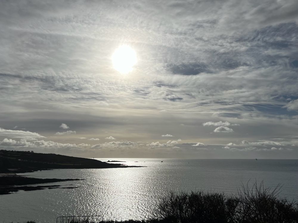 The sun shining on the sea on a cloudy day.  The sunlight is muted in the sky.