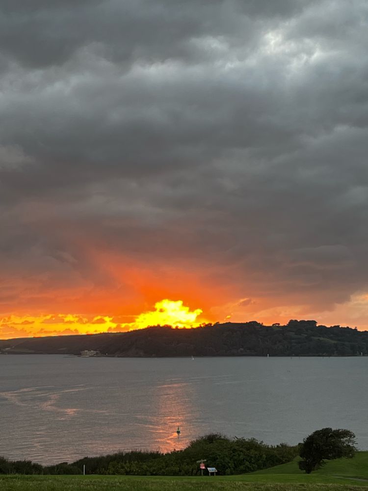 The sun setting over land with the orange rays on the see.  