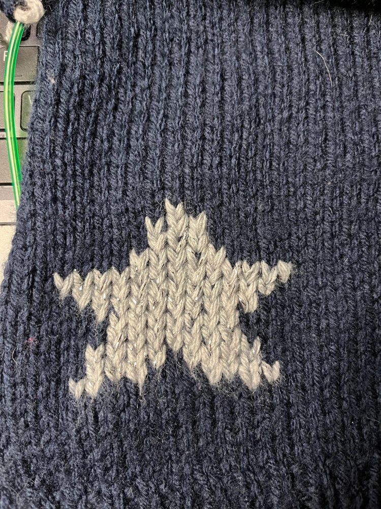 Kind of wonky duplicate knit star in silver yarn on a background of navy blue yarn