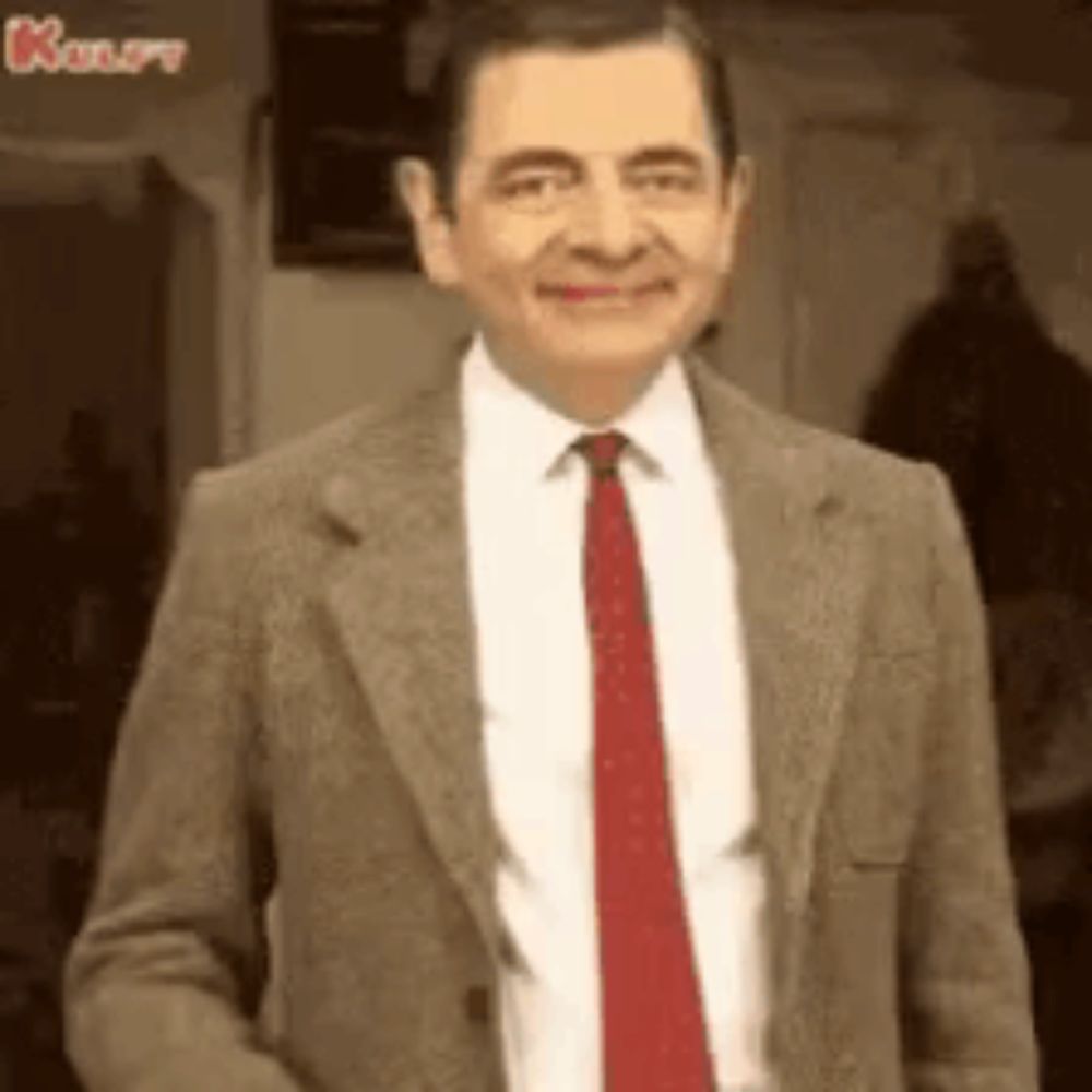 mr bean is wearing a suit and tie and smiling at the camera .