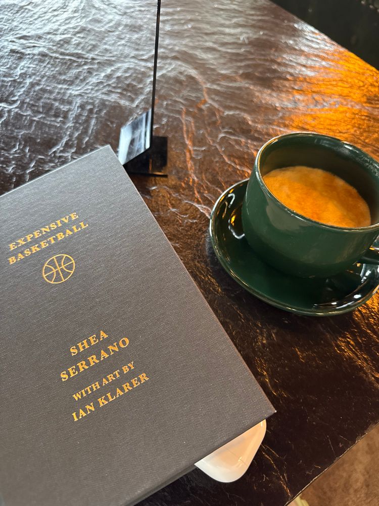 A cup of cappuccino next to Shea Serrano’s hardcover book “expensive basketball”