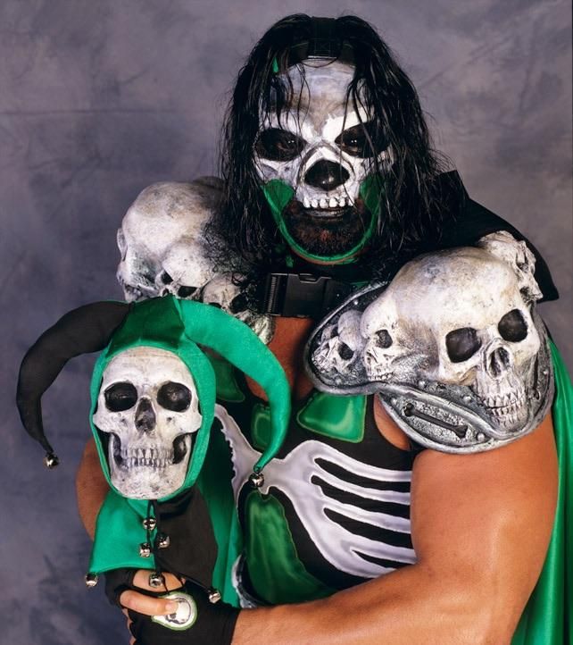 mortis from WCW, a man in a skull mask with skull pauldrons, holding a staff with a skull on it that's wearing a jester mask