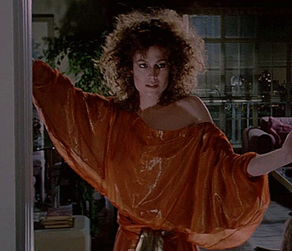 a woman with curly hair is standing in front of a window with her arms outstretched