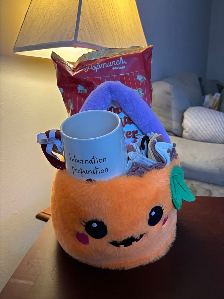 a boo basket in a pumpkin bucket with a smiley face that consists of socks, a mug, & popcorn 