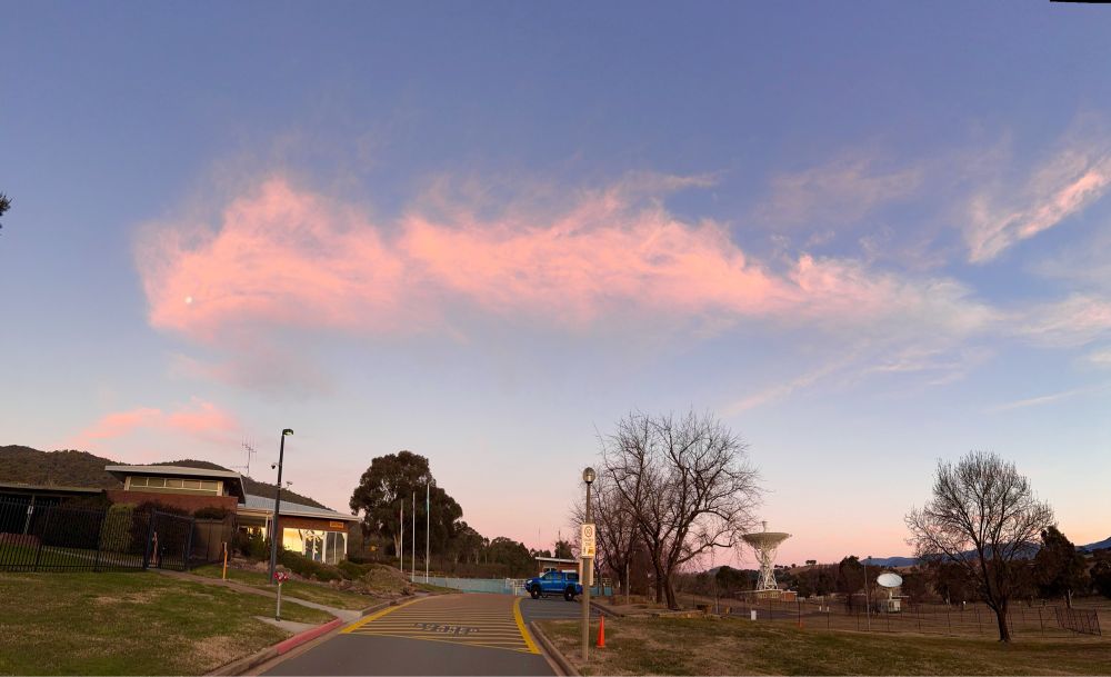 A wide view of the Moon surrounded by a long wispy cloud that looks pinkish with the setting sun.