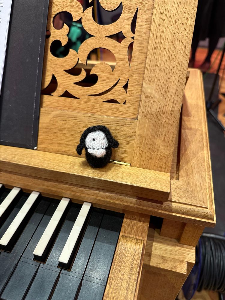 A close up of a small knitted nun on the music desk of the chest organ.