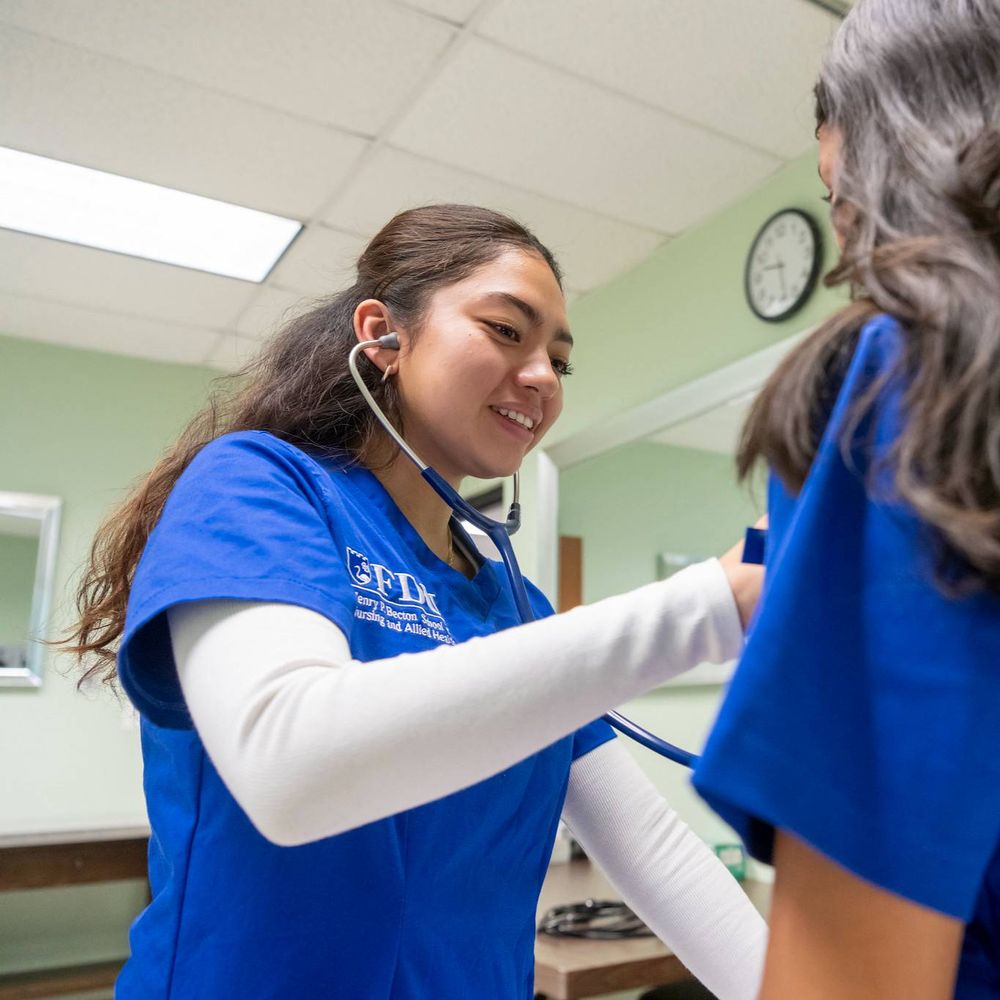 A student uses a stethoscope in class, examining another student.