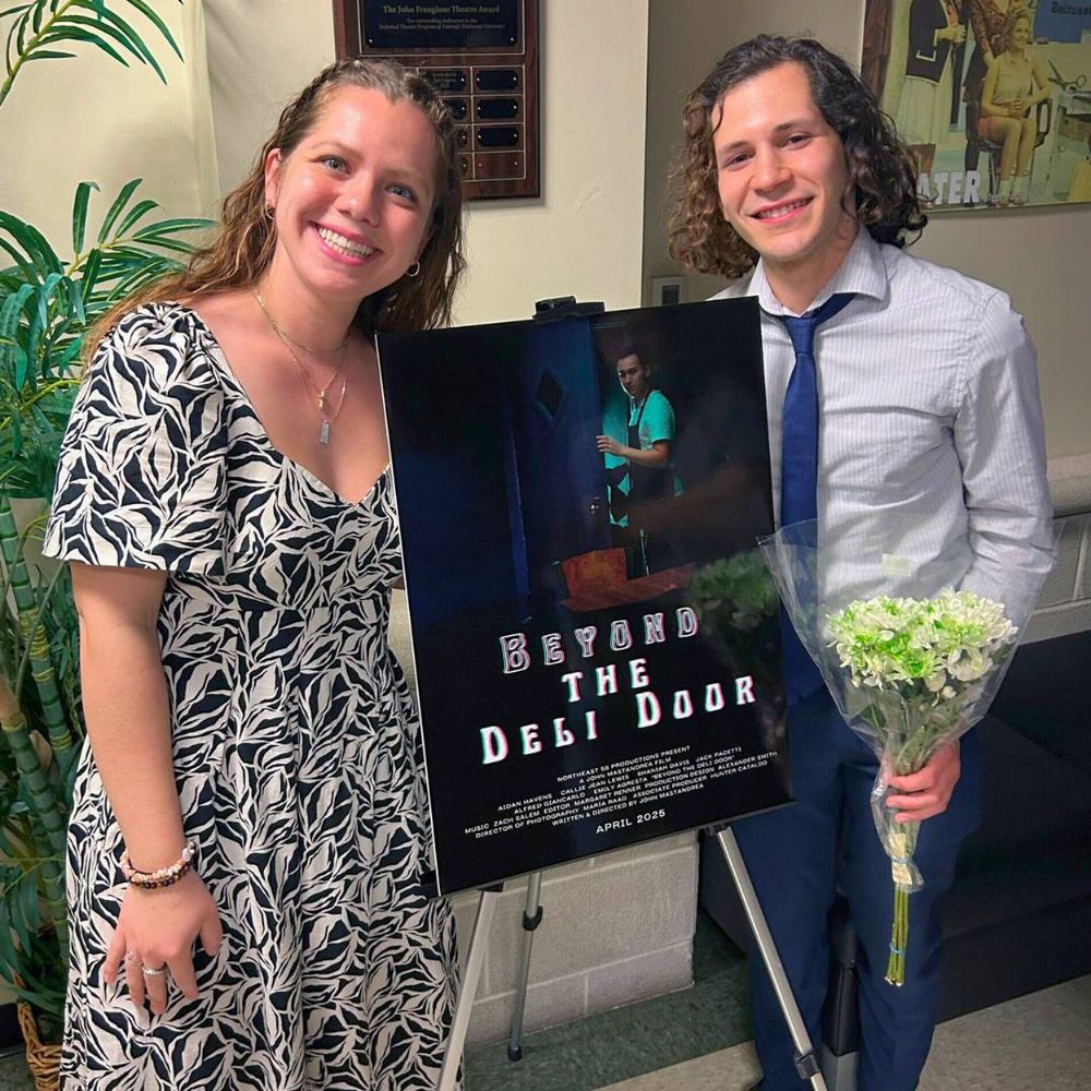 A woman and a man pose with a film poster. the poster reads "beyond the deli door."