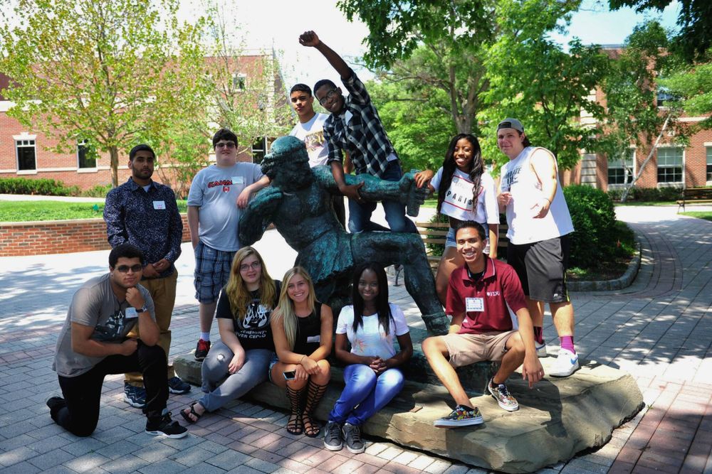 a group of FDU students pose around a statue. one student excitedly pumps his fist into the air.
