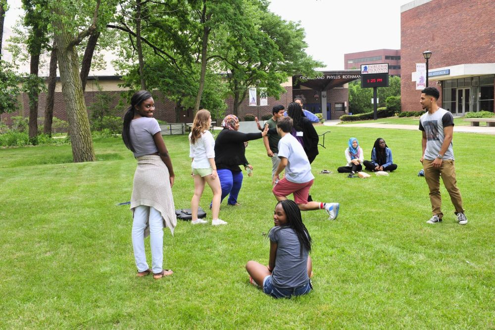 a group of FDU students plays a game on a college campus lawn. one student smiles are the camera.