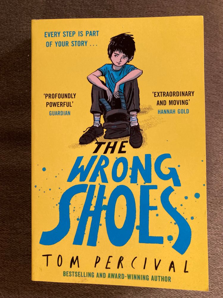 A copy of The Wrong Shoes, by Tom Percival. The cover illustration is a drawing of a young boy sitting down with a rucksack.

This was recommended to me by a friend and I’ve just finished it. It’s the story of a boy whose poverty makes it hard for him to manage and fit in at school. It’s a very powerful depiction of how poverty impacts so many areas of a child’s life, and the difficult choices Will has to make, but all folded into a compelling story with characters it’s easy to care about. The book is beautifully illustrated too, by the author.