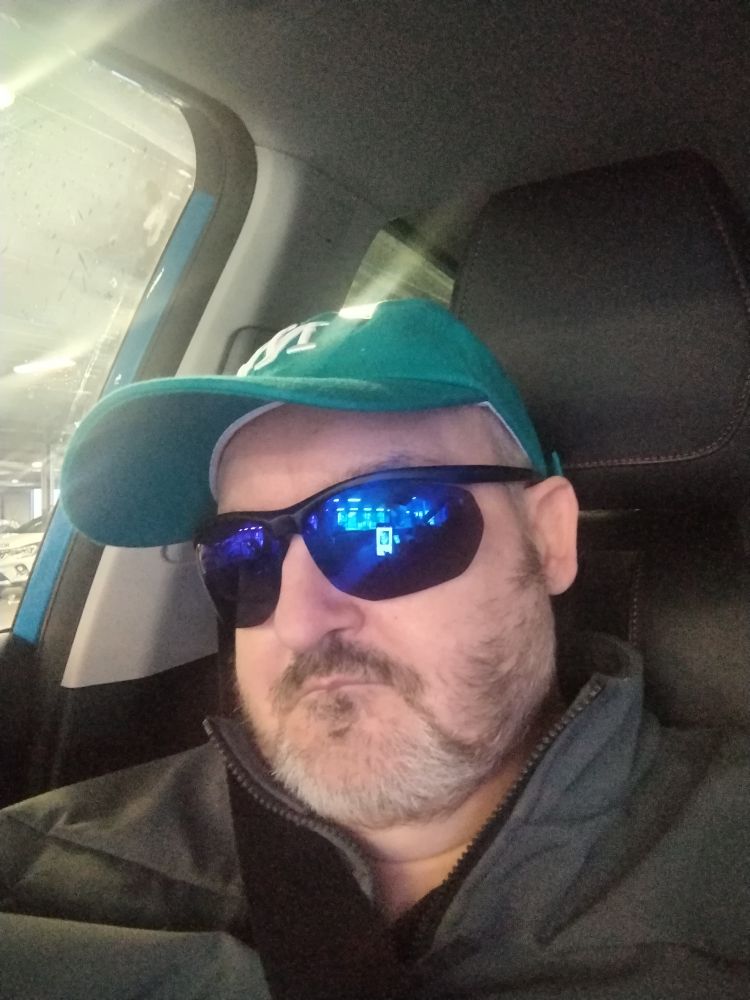 A man sat in a car with a grey coat and a new pair of distance sunglasses. 