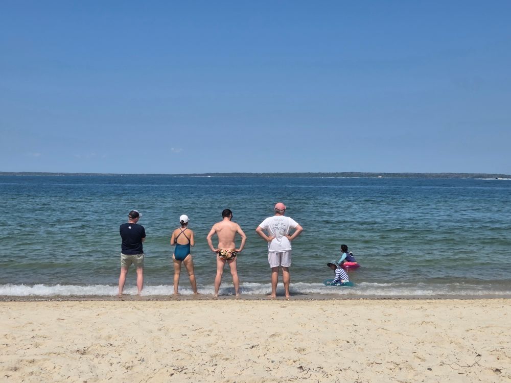 Four people stand in a row at Lambert’s Cove Beach in West Tisbury, MA. 