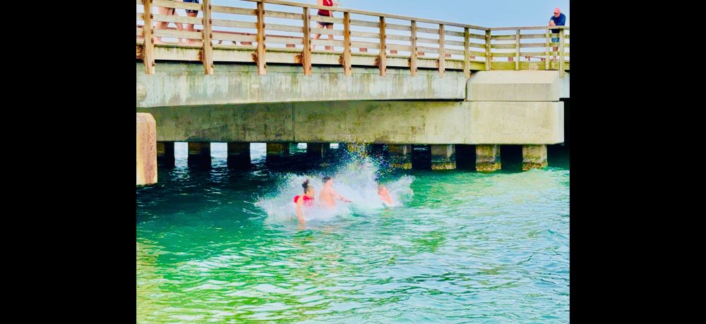 Four people hitting the water after jumping off the bridge above them. 