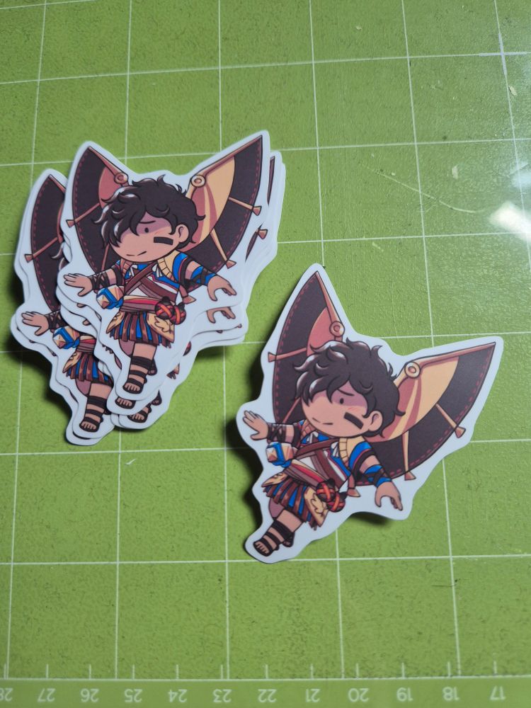 A stack of stickers of a chibified Icarus from Hades II on a cricut mat.