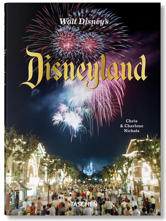 Photo of a book cover that shows a street of Disneyland lit up brightly at night as crowds walk down it. A fairy tale castle can just be seen far in the distance. Massive fireworks explode overhead, with the titled laid out in gold over them. Title: Walt Disney's Disneyland by Chris & Charlene Nichols TASCHEN logo at bottom.