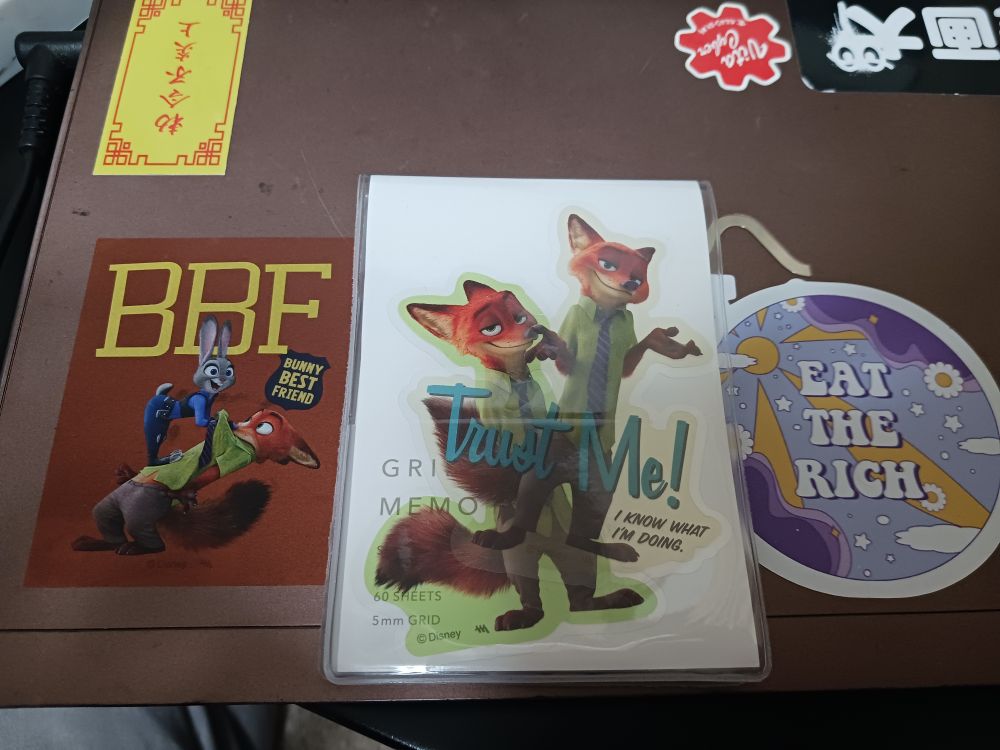 シールが色々貼られたノートパソコン。左にBBF,BUNNY BEST FRIENDと書かれたジュディとニックのクリアオレンジ色のステッカー、中央にニックのダイカットステッカーを2枚カバーに挟んだメモ帳