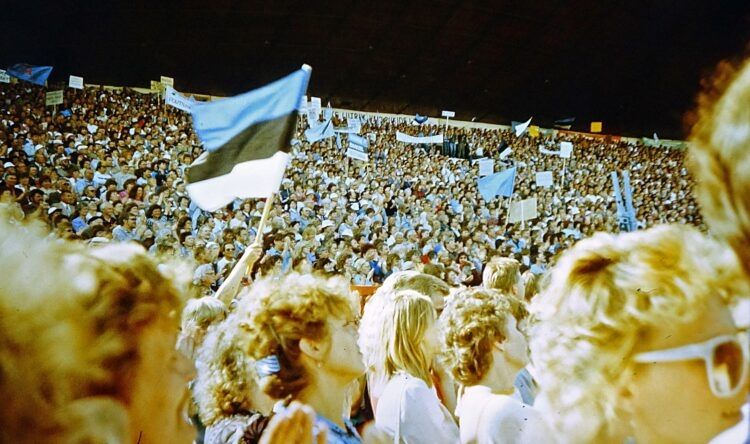 A crowd of people sing during Estonia's Singing Revolution. Some wave Estonian flags.