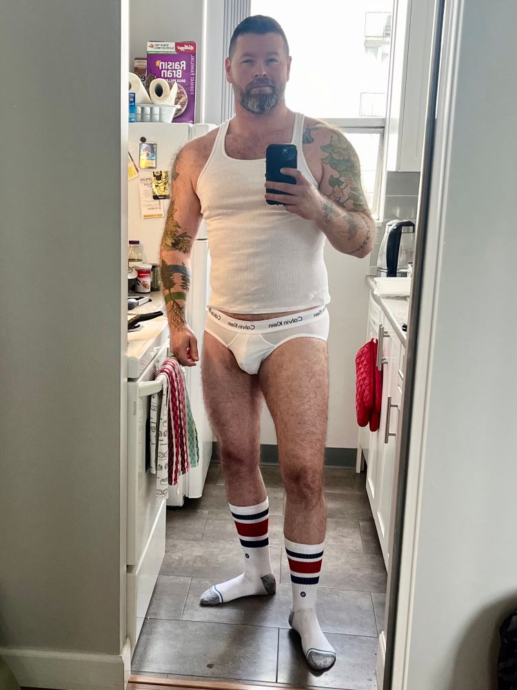 Bearded man in briefs, socks and t shirt taking a cheeky mirror selfie.