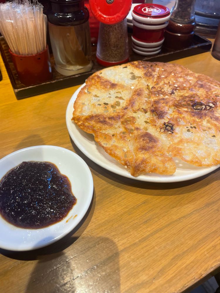 A plate of fried gyoza with a dish of dipping sauce next to it.