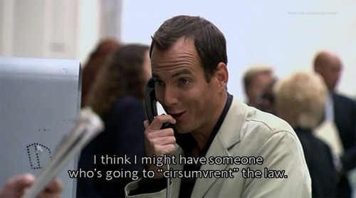 Gob stands at a payphone, smirking mischievously as he speaks into the receiver. He wears a light-colored jacket and looks pleased with himself, clearly enjoying whatever scheme he’s referencing. His expression is confident, with a raised eyebrow and a glint of self-satisfaction. People blur in the background, placing him in a public setting.