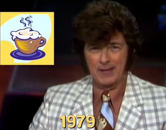 John Beard in a retro 1979 news segment, wearing a large brown wig, thick sideburns, a light plaid blazer, and a wide brown-and-blue tie. A cartoon image of a steaming cup of coffee appears in the top left corner. The year “1979” is displayed in bold yellow text at the bottom.
