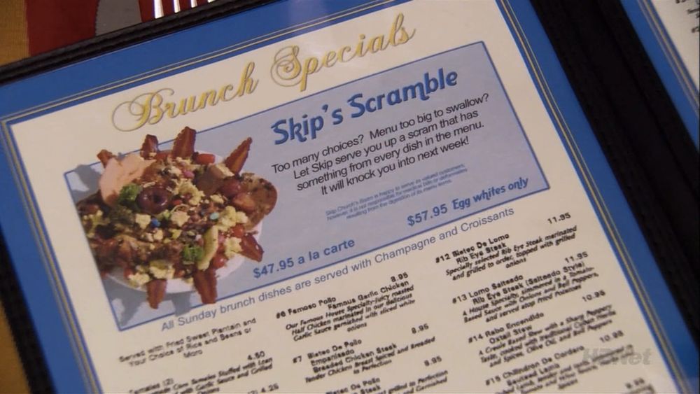 A close-up of a brunch menu showcases the extravagant “Skip’s Scramble,” a chaotic mountain of food featuring eggs, bacon strips, olives, broccoli, chunks of meat, multicolored candy pieces, and various unidentifiable toppings piled high on a plate. The dish is marketed as a catch-all combo—“something from every dish in the menu”—with the promise it will “knock you into next week.” Prices range from $47.95 à la carte to $57.95 for egg whites only. The presentation and pricing are absurdly over-the-top, fitting the show’s satirical tone.