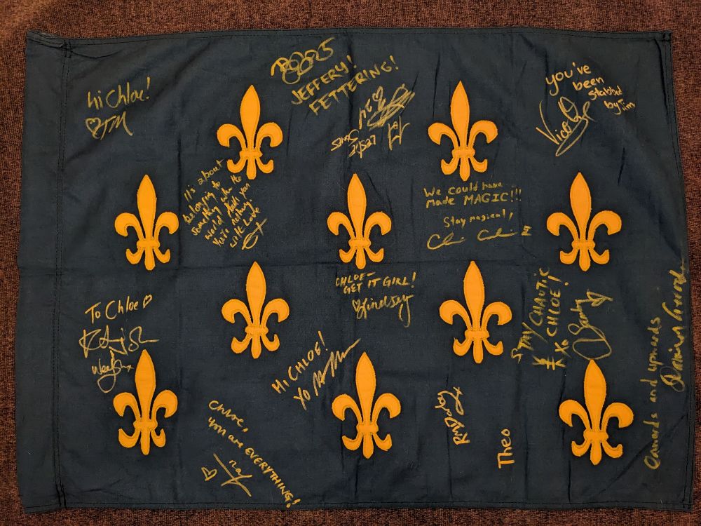 A navy blue flag with gold fleur-de-lis symbols on it, signed by members of the cast and crew of Our Flag Means Death 