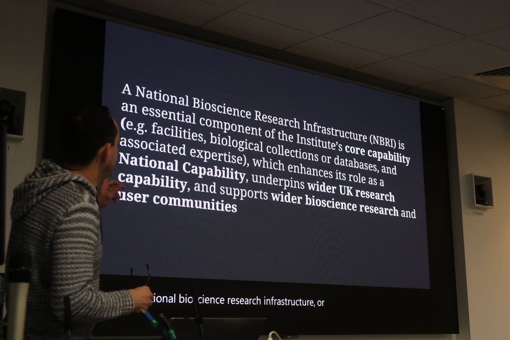 A presentation screen describing what a National Bioscience Research Infrastructure is: "A National Bioscience Research Infrastructure (NBRI) is an essential component of the Institute's core capability (e.g. facilities, biological collections, or databases, and associated expertise), which enhances its role as a National Capability, underpins wider UK research capability, and supports wider bioscience research and user communities."