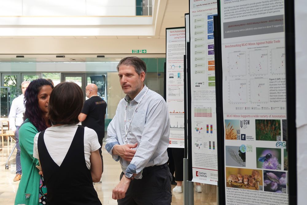 Attendees chatting in the Earlham Institute Atrium besides a display of scientific posters.
