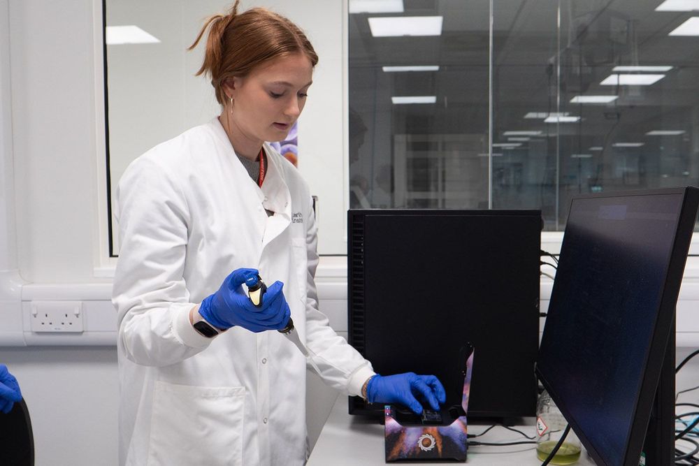 TLevel student Rosie working in the genomics labs at the Earlham Institute wearing a white lab coat and blue safety gloves.