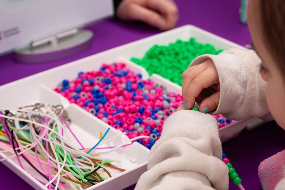 Close up of a child's hand adding colourful beads to the keyring they're making.