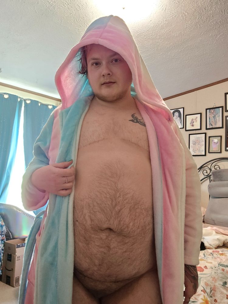 Bee wearing a plush trans colored robe with hood, open to show their top surgery scars, belly, and bush